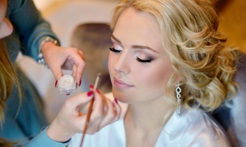 Wedding makeup artist making a make up for bride. Beautiful sexy model girl indoors. Beauty woman with curly hair. Female portrait. Bridal morning of a cute lady. Close-up hands near face